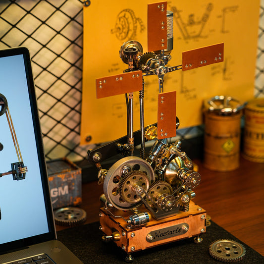 A steampunk-style mechanical model with gears, brass-toned metal parts, and orange-brown rectangular plates, displayed on a tabletop. A laptop is partially visible on the left, and industrial-style containers and a yellow backdrop are in the background.