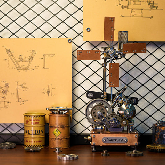 A steampunk-style mechanical sculpture or model on a wooden base, displayed on a tabletop with metal cans, gears, and blueprint posters against a diamond-pattern backdrop.